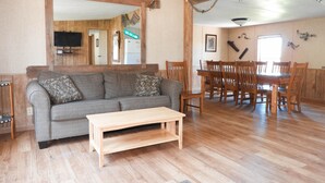 Una sala de estar con un sofá gris, una mesa de centro de madera y una zona de comedor con sillas y mesa de madera.