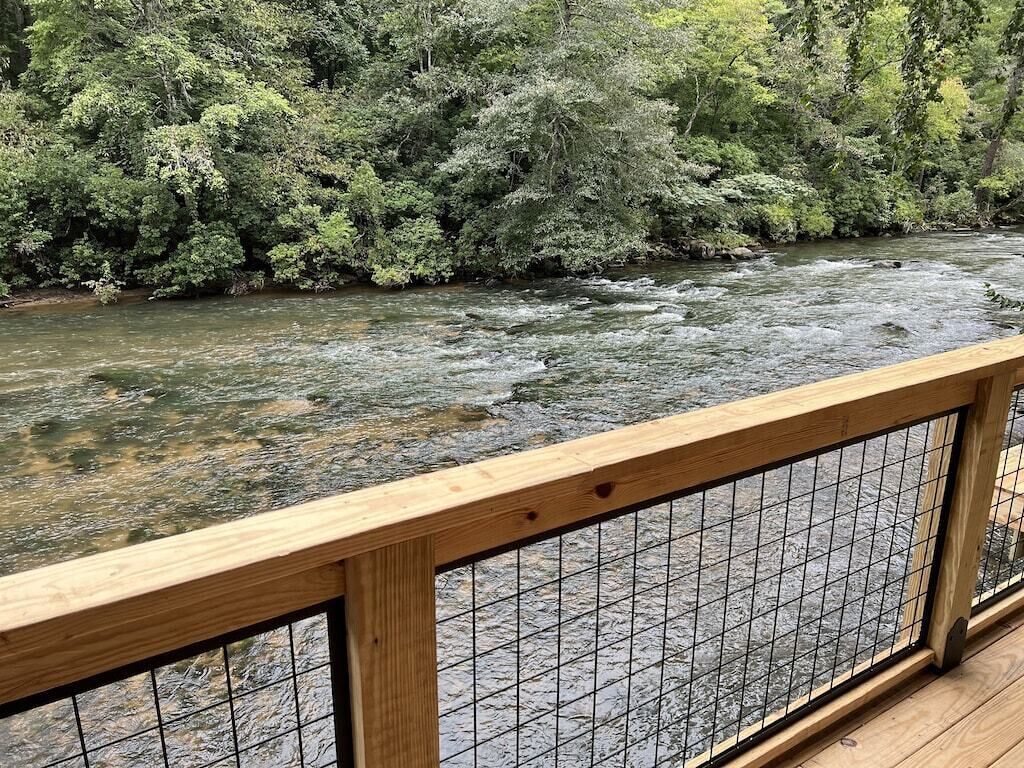 A wooden deck with a metal railing overlooking a river.
