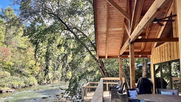 Een houten terras met rieten meubilair met uitzicht op een rivier, omgeven door bomen.