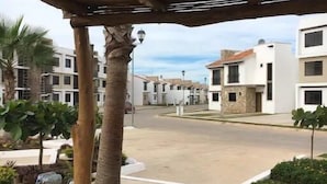 A covered outdoor area with a concrete floor, palm trees, and a view of residential buildings in the background. - Departamentos Pacific Blue (Mazatlán)