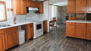 A kitchen with wooden cabinets, a white stove, and a stone accent wall. - Sunset Ridge perfect vacation home near Meramec River (Leasburg)
