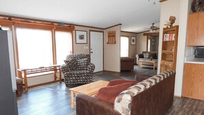 A spacious living room with a brown sofa, a patterned armchair, and a wooden coffee table. There is a dining area with a bench and a table, and a kitchen area with wooden cabinets and a microwave. - Sunset Ridge perfect vacation home near Meramec River (Leasburg)