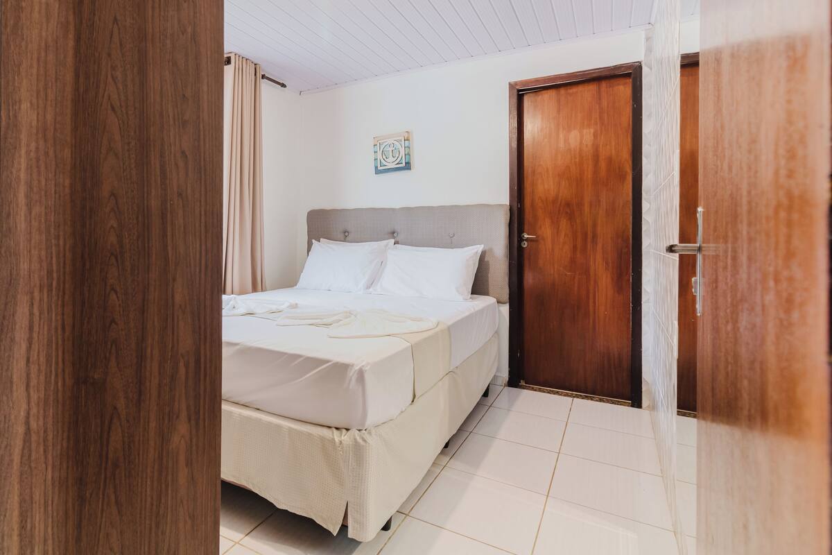 Um quarto com cama, porta de madeira e teto branco.