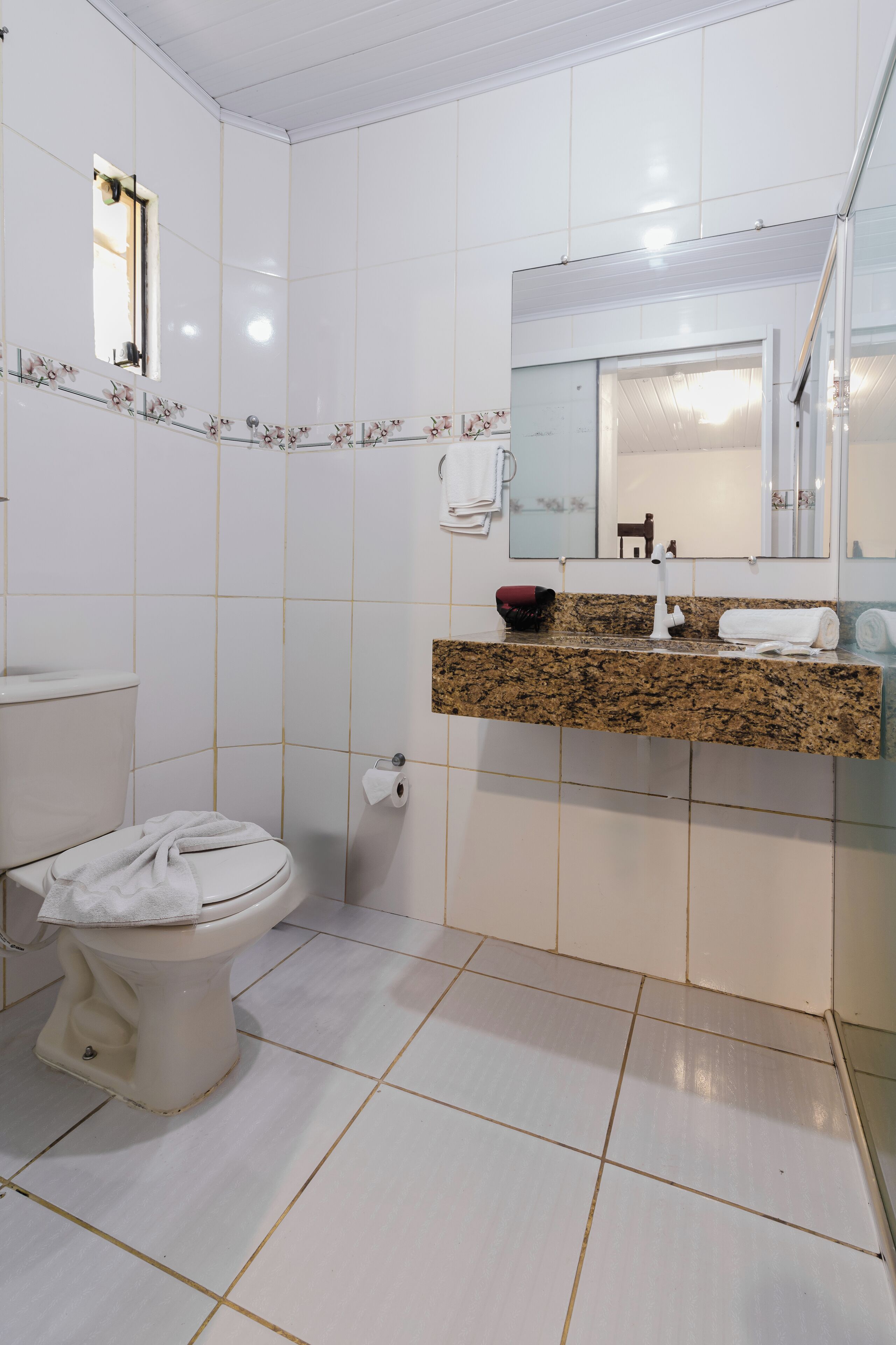 Un baño con inodoro, lavamanos y encimera de granito, y un espejo sobre el lavamanos.