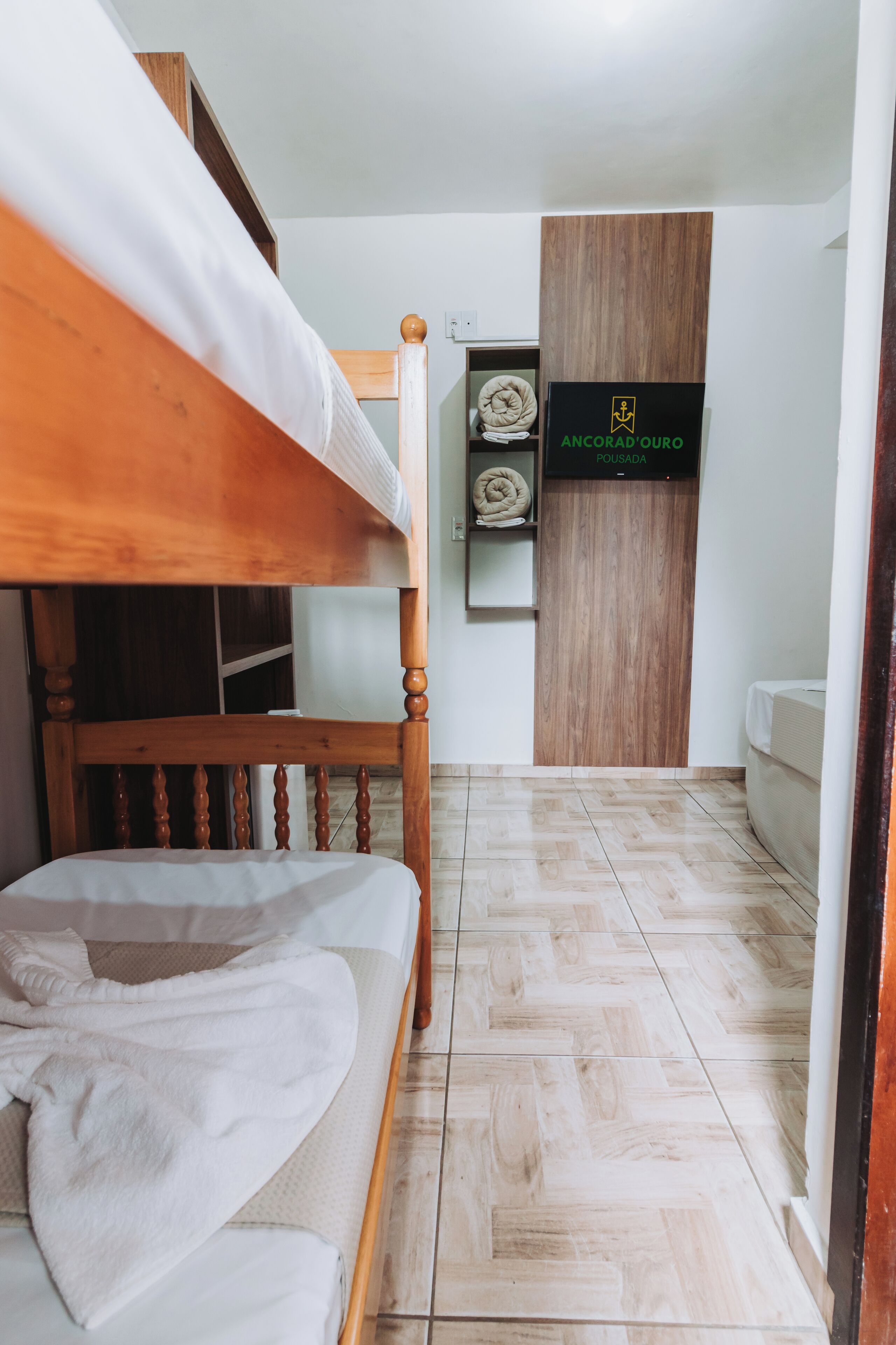 Una cama litera con cabecera de madera, un pequeño estante con una toalla enrollada y una puerta de madera con un cartel.