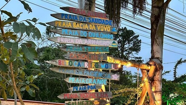 A wooden signpost with multiple directional signs, a large anchor sculpture, and a rustic wooden wall in the background. - Ancoradouro Pousada (Penha)