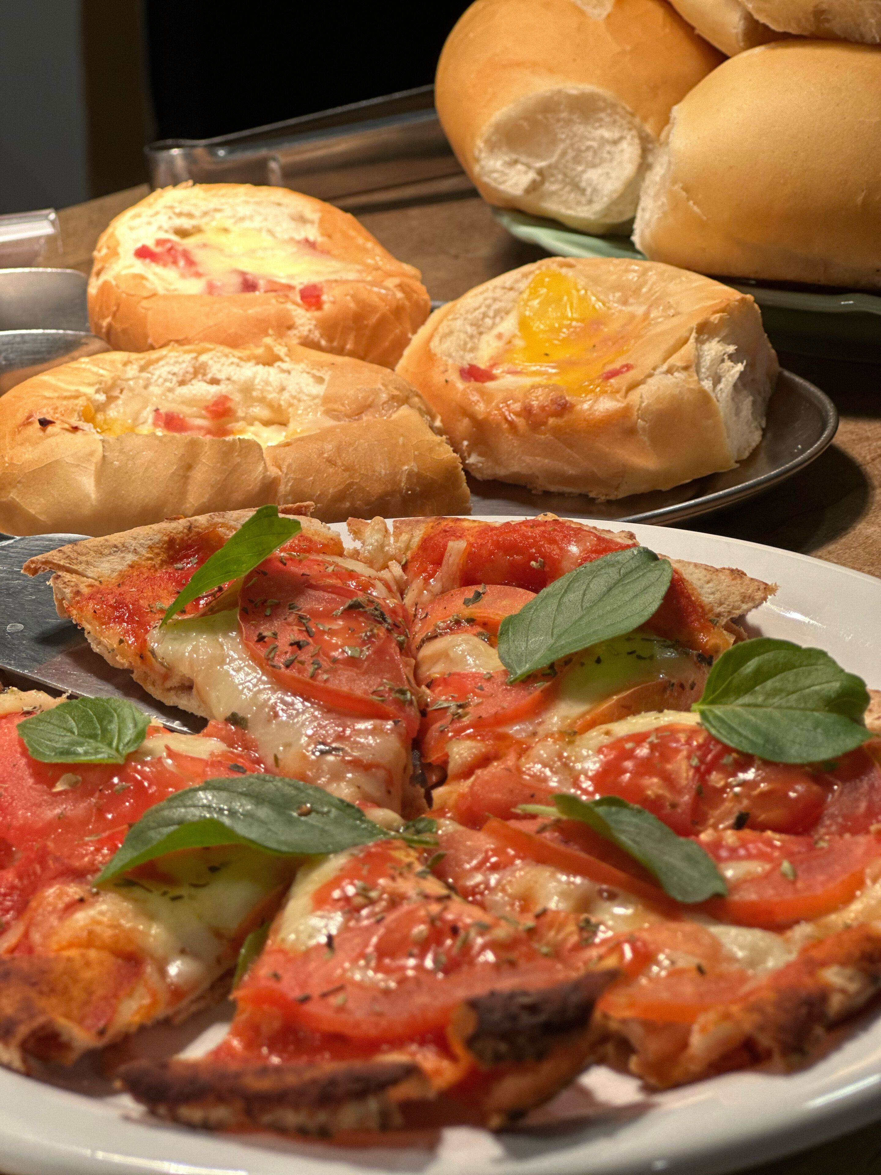 Pizza com cobertura de tomate e queijo, decorada com folhas de manjericão, sobre um prato branco.
