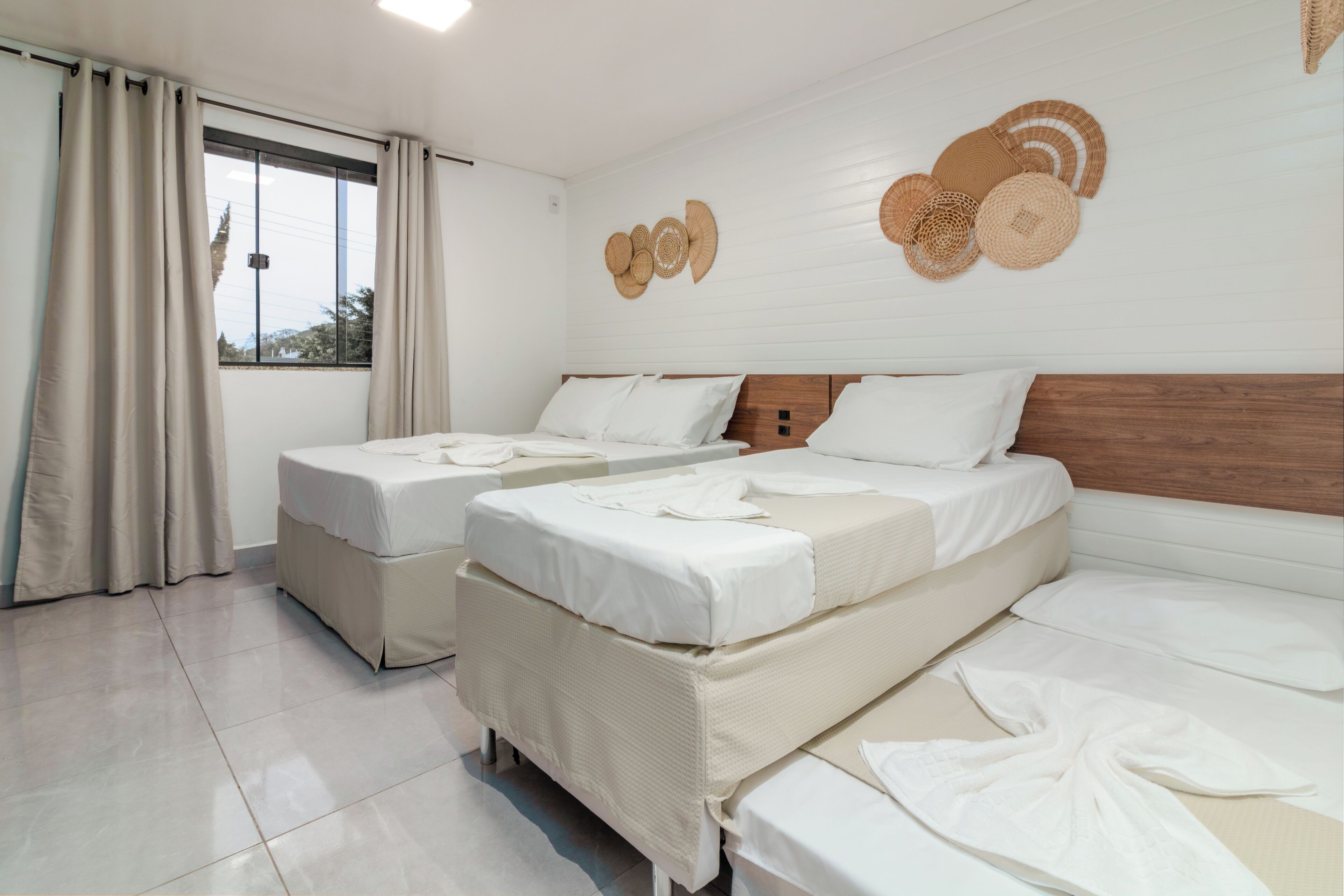 A hotel room with two beds, a large window with curtains, and wall decor.