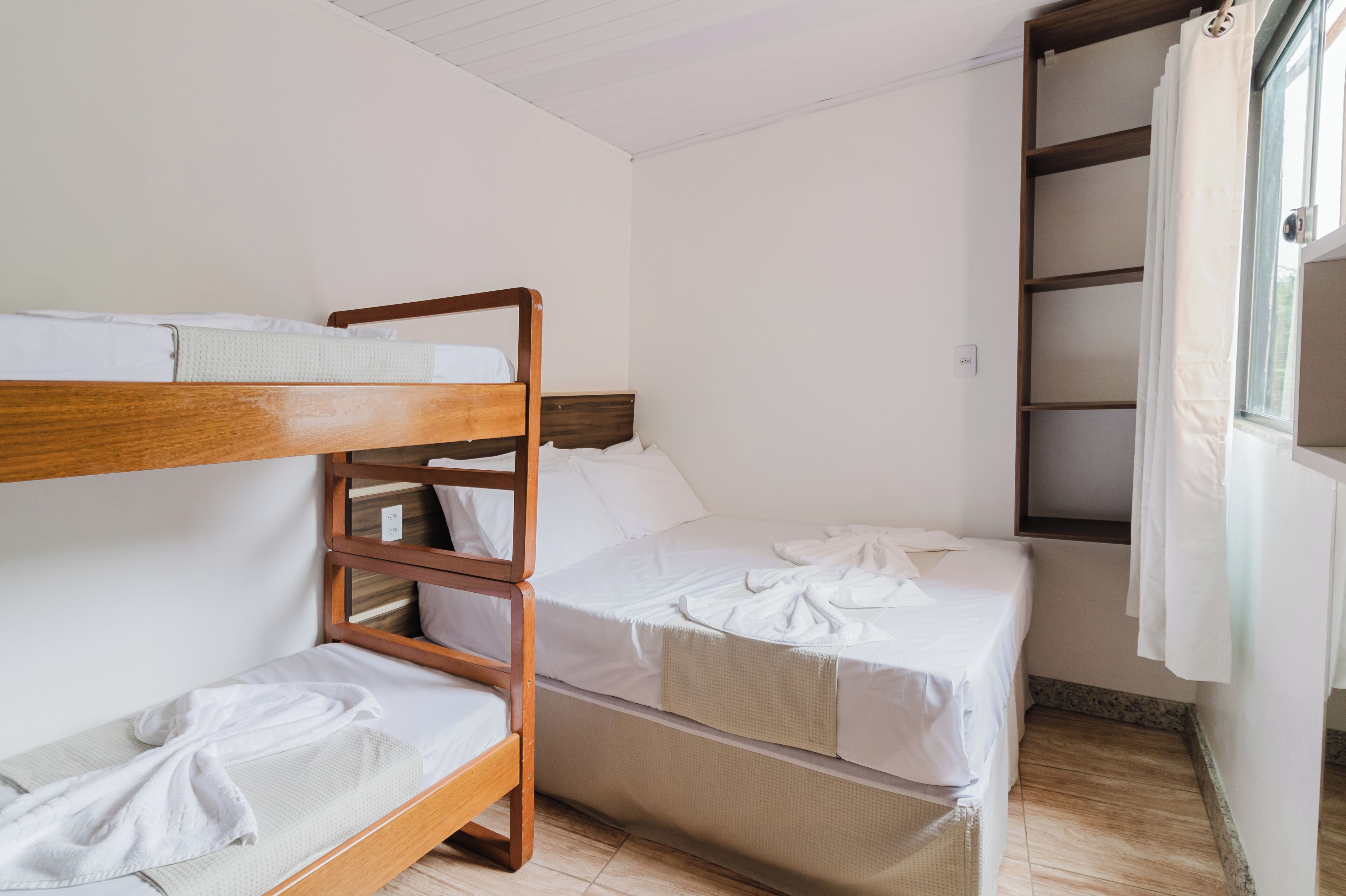 A bunk bed room with a wooden headboard, a small table, and a window with curtains.