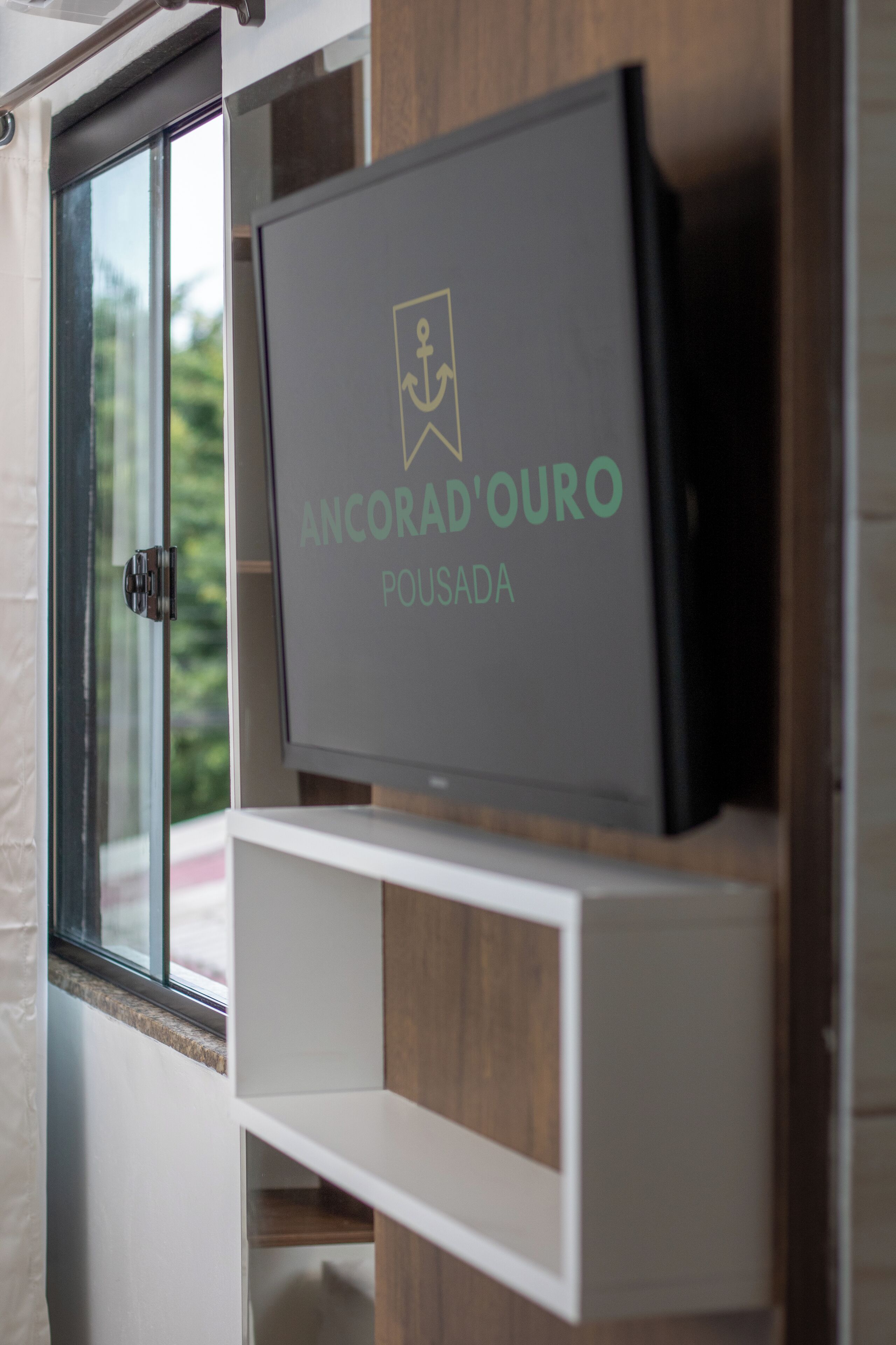 A television mounted on a wooden wall with a window to the left.