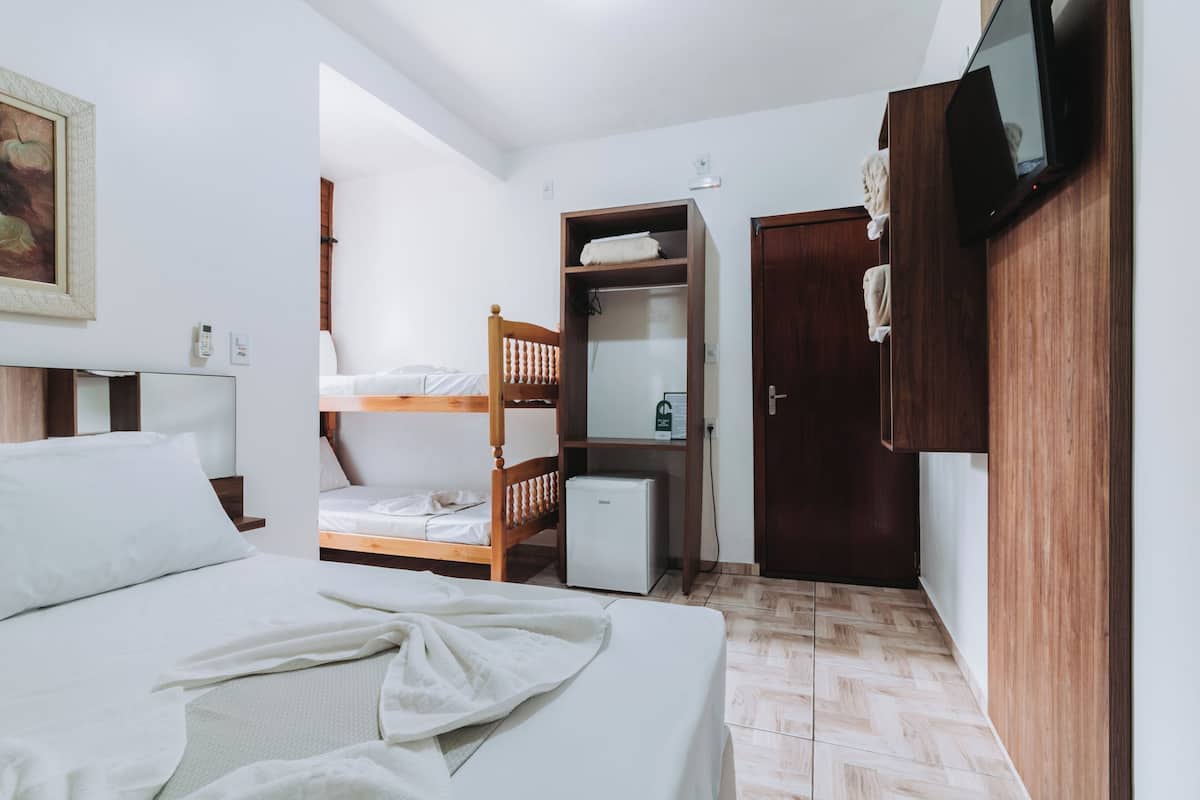 Quarto com beliche, pequena geladeira, guarda-roupa de madeira e televisão fixada na parede.