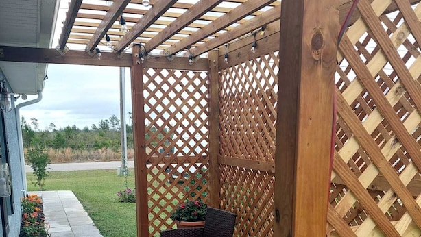 Ein überdachter Patio-Bereich mit Korbmöbeln und einem kleinen Tisch, umgeben von einem Holzzapfenzaun.