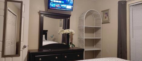 A bedroom with a bed, dresser, mirror, television, and a decorative arched shelf.