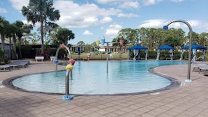 Ein Swimmingpool mit kreisförmigem Rand, umgeben von Palmen und blauen Markisen.