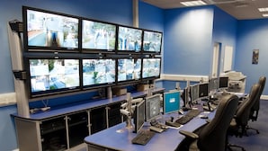 Een controlekamer met meerdere monitoren waarop camerabeelden te zien zijn, een bureau met computers en bureaustoelen.