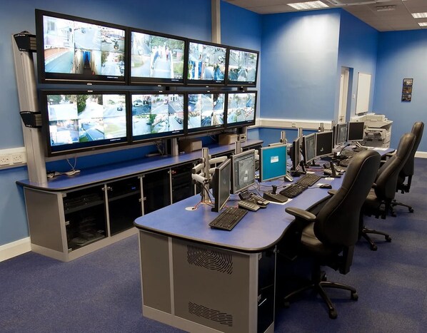 A control room with multiple monitors displaying surveillance footage, a desk with computers, and office chairs. - Immaculate 3-bed House in Lahore Near Airport (Lahore)
