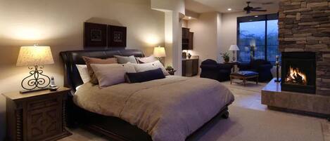 A bedroom with a large bed, a fireplace, and a view of the outdoors.