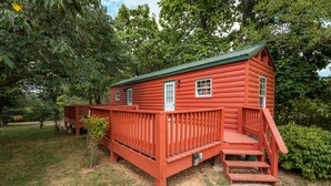 Une cabane en rondins rouge avec un toit vert, une terrasse en bois et un petit porche.