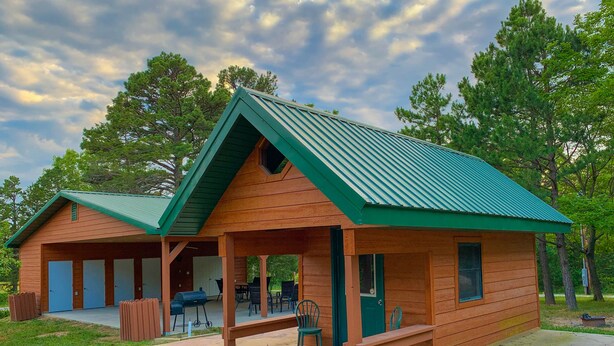 Une cabane en bois avec un toit vert, une véranda avec des sièges et un espace barbecue.