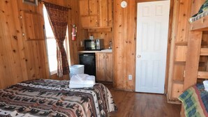 Une pièce dans un chalet en bois, comprenant un lit, une petite kitchenette et une porte.