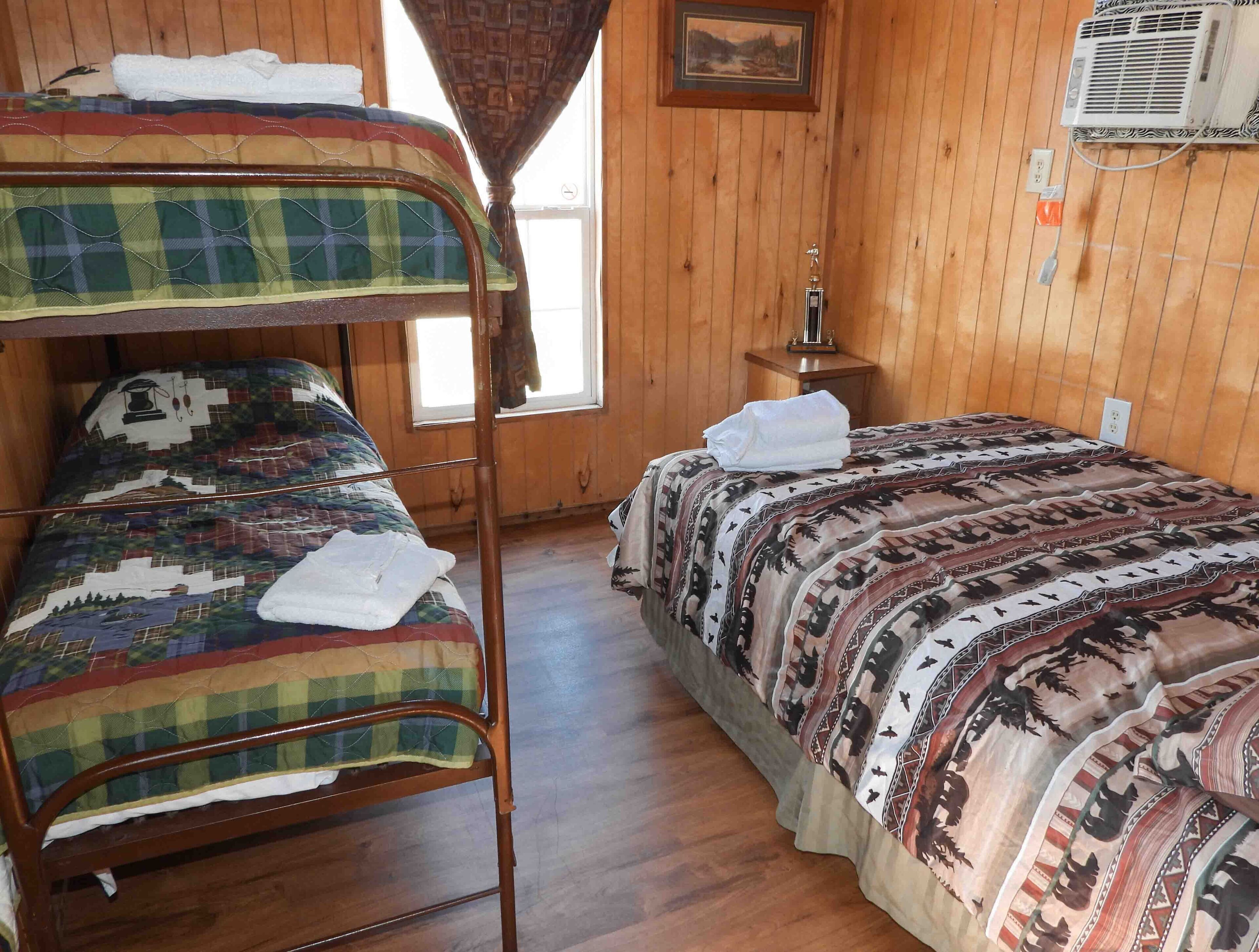 Een kamer met een stapelbed, een enkel bed, houten wanden, een raam en een airconditioning.