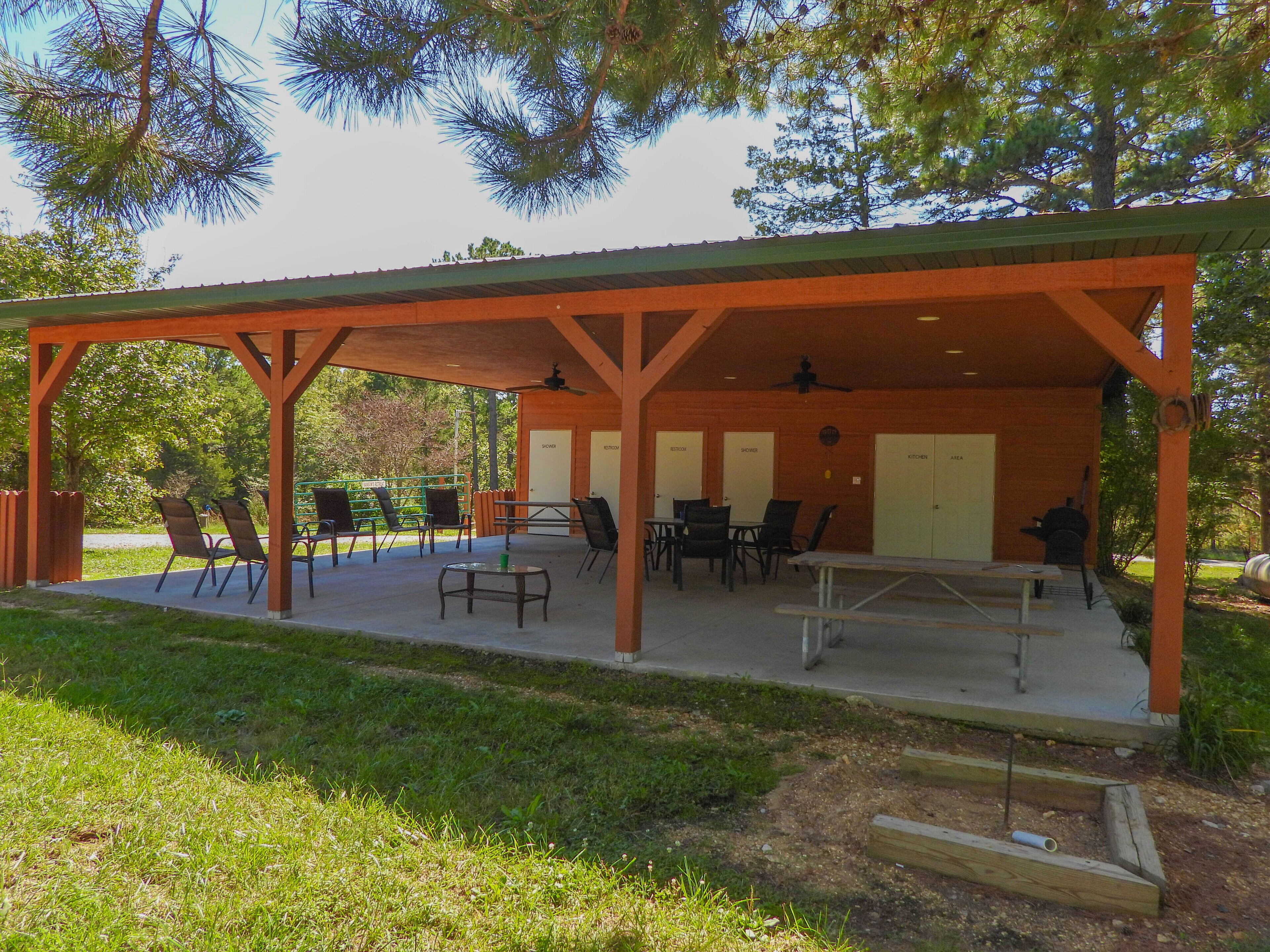 Un espacio al aire libre techado con mesas y sillas de picnic, una parrilla y un pequeño jardín.