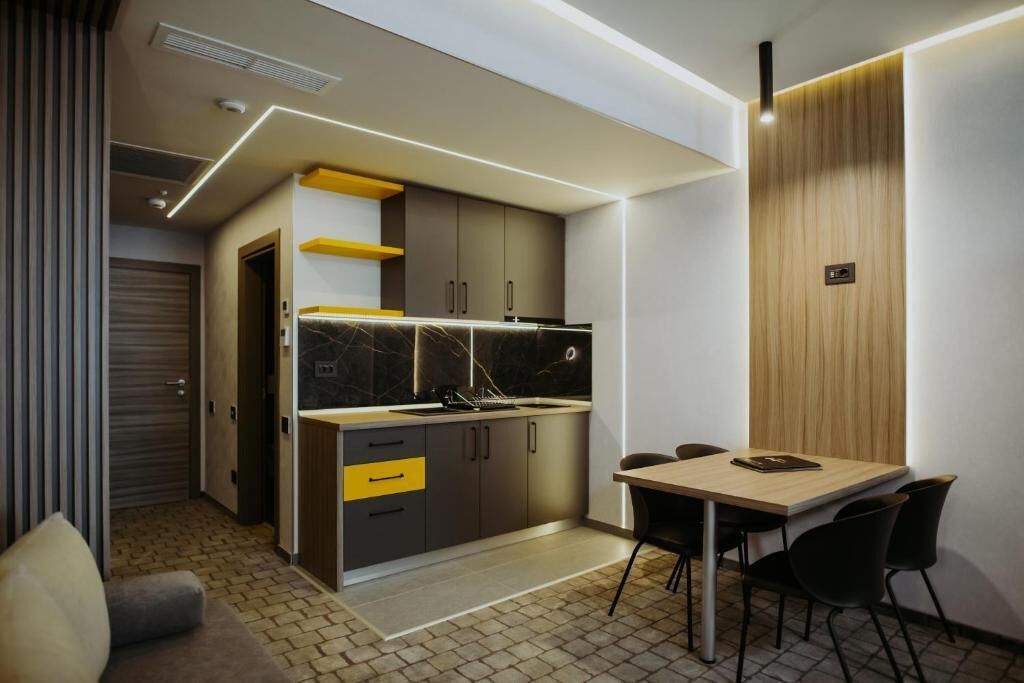 Una cocina compacta con electrodomésticos modernos, un área de comedor con mesa y sillas, y una pared de acento de madera.