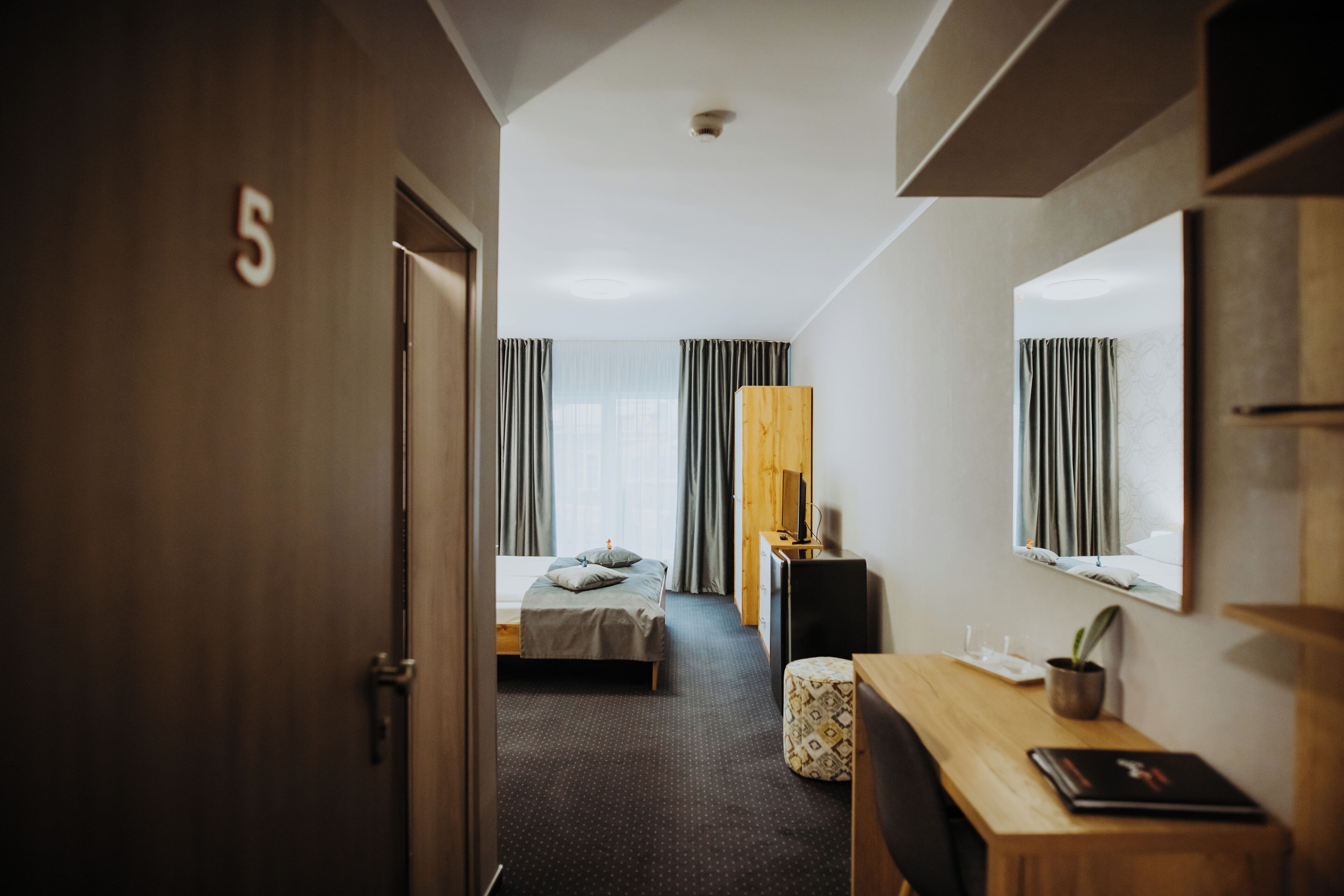 A hotel room with a bed, a desk, a chair, a television, and a window with curtains.