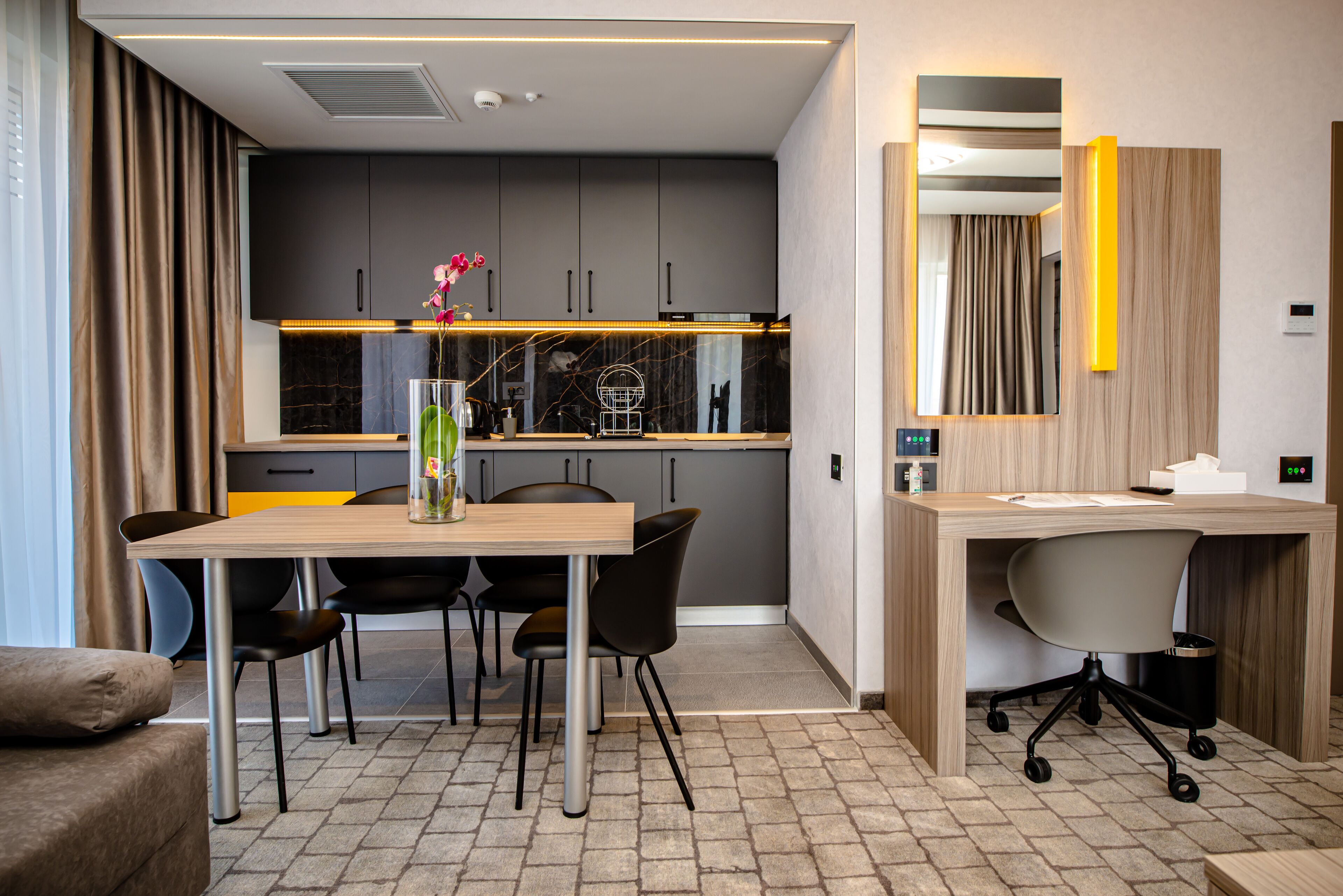 A modern hotel room with a dining area, a wooden desk, and a large mirror.