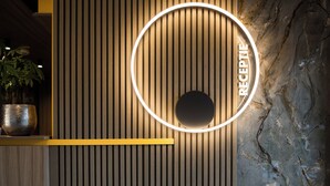 Zona de recepción con listones de madera verticales, pared de mármol y un letrero circular iluminado.