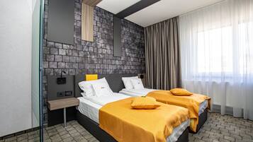 A modern hotel room with two beds, a stone accent wall, a bedside table, and a large window with curtains.