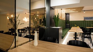 Un interior de restaurante moderno con mesas de madera, sillas negras y asientos tapizados en tonos verdes.