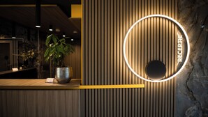 Un mostrador de recepción con una planta en maceta, un letrero circular iluminado y una pared de mármol.