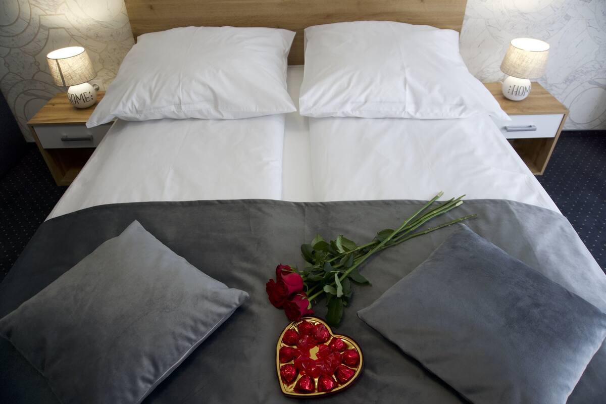 A neatly made bed with white linens, two bedside tables with lamps, and a bouquet of red roses on the bed.