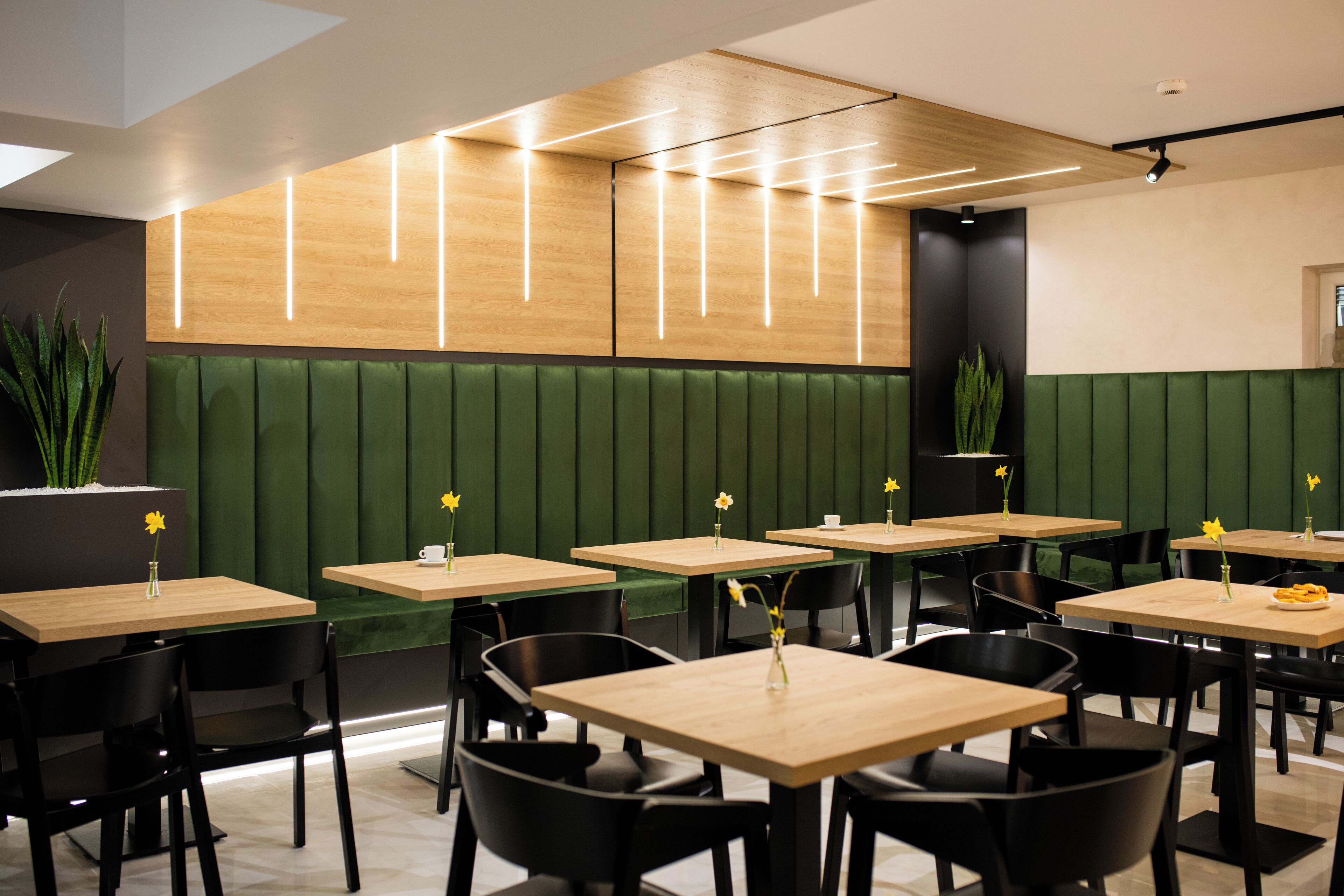 Interior moderno de restaurante con asientos tipo banca verdes, mesas de madera y sillas negras.