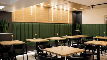 Interior moderno de restaurante con asientos tipo banca verdes, mesas de madera y sillas negras.