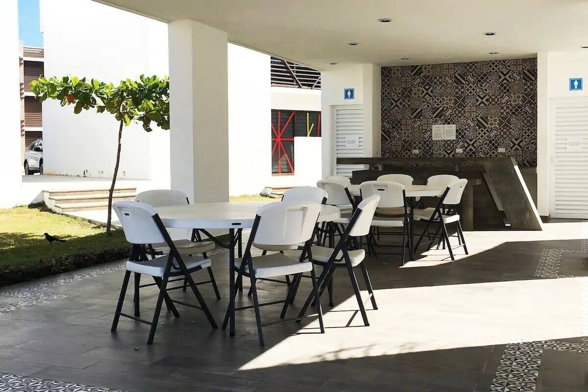 An outdoor dining area with white tables and chairs, a patterned wall, and a staircase leading to an upper level.