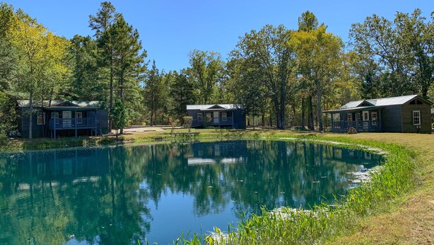 A lakeside cabin with a dock, surrounded by trees and a clear blue sky. - Fletcher's Village Group Cabin rental near Meramec River. (Leasburg)