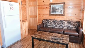 A wooden cabin interior with a white refrigerator, a brown leather sofa, and a patterned throw blanket. - Fletcher's Village Group Cabin rental near Meramec River. (Leasburg)