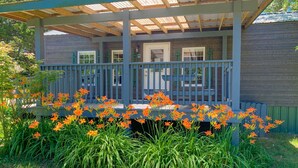 A wooden cabin with a porch, surrounded by tall grass and orange flowers. - Fletcher's Village Group Cabin rental near Meramec River. (Leasburg)