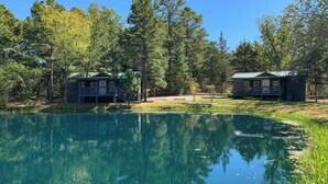 A lakeside cabin with a dock, surrounded by dense forest and clear blue sky. - Fletcher's Village Group Cabin rental near Meramec River. (Leasburg)