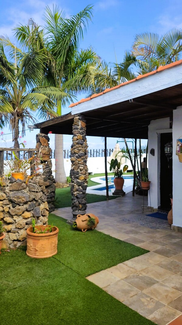 A covered patio area with stone pillars, potted plants, and a pool in the background.