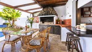 A kitchen with a stone fireplace, wooden ceiling, and a dining area with wicker chairs and a glass table. - Casa Cateyma with pool (Icod de los Vinos)