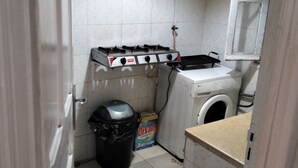 Eine kleine Küche mit Gaskochfeld, Waschmaschine und Mülleimer.
