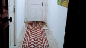 Ein schmaler Korridor mit einem gemusterten Boden, einer weißen Tür am Ende und einem Gemälde an der Wand.