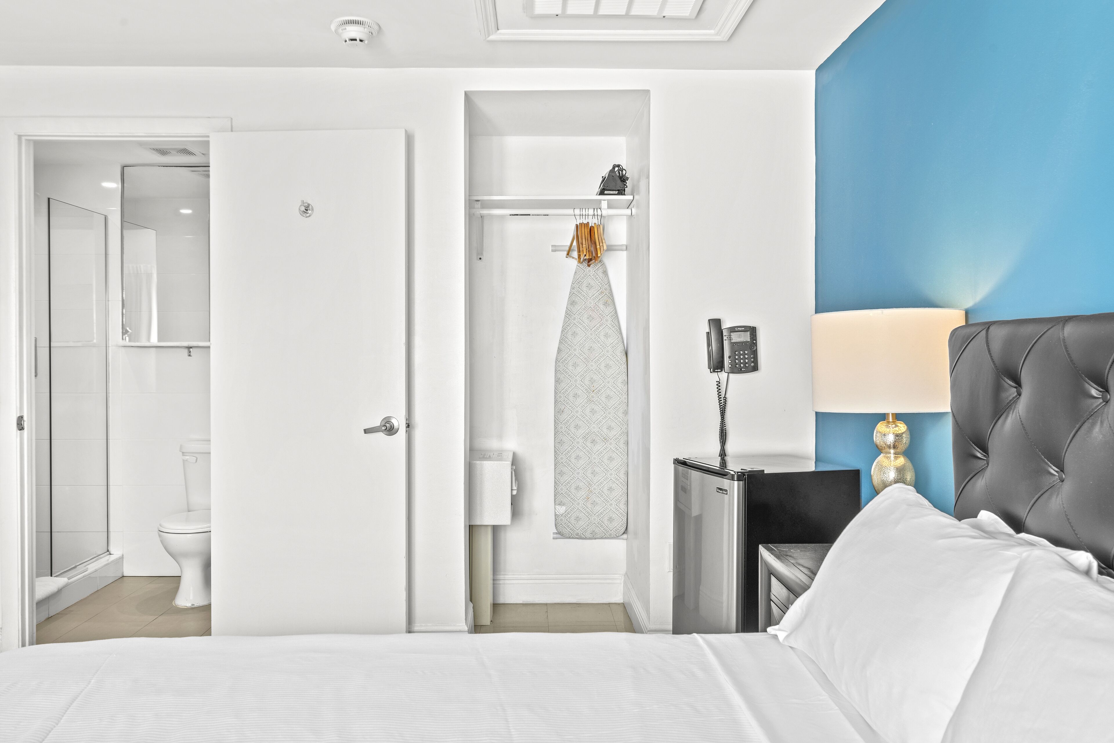 Ein Hotelzimmer mit einem Bett, einem Nachttisch mit Lampe, einem Telefon, einem Badezimmer mit Toilette und einer Duschkabine.
