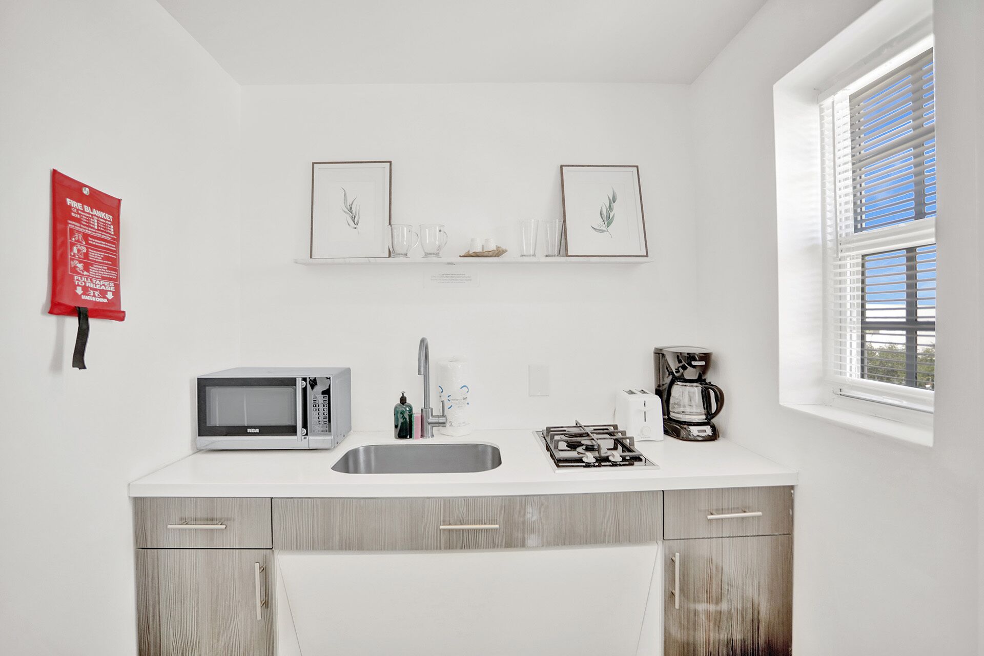 Eine moderne Küche mit Mikrowelle, Kaffeemaschine und Spüle. Über der Arbeitsfläche hängen zwei gerahmte Bilder an der Wand.