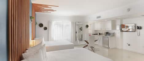 A modern hotel room with two beds, a kitchenette, a bathroom, and a large mirror.