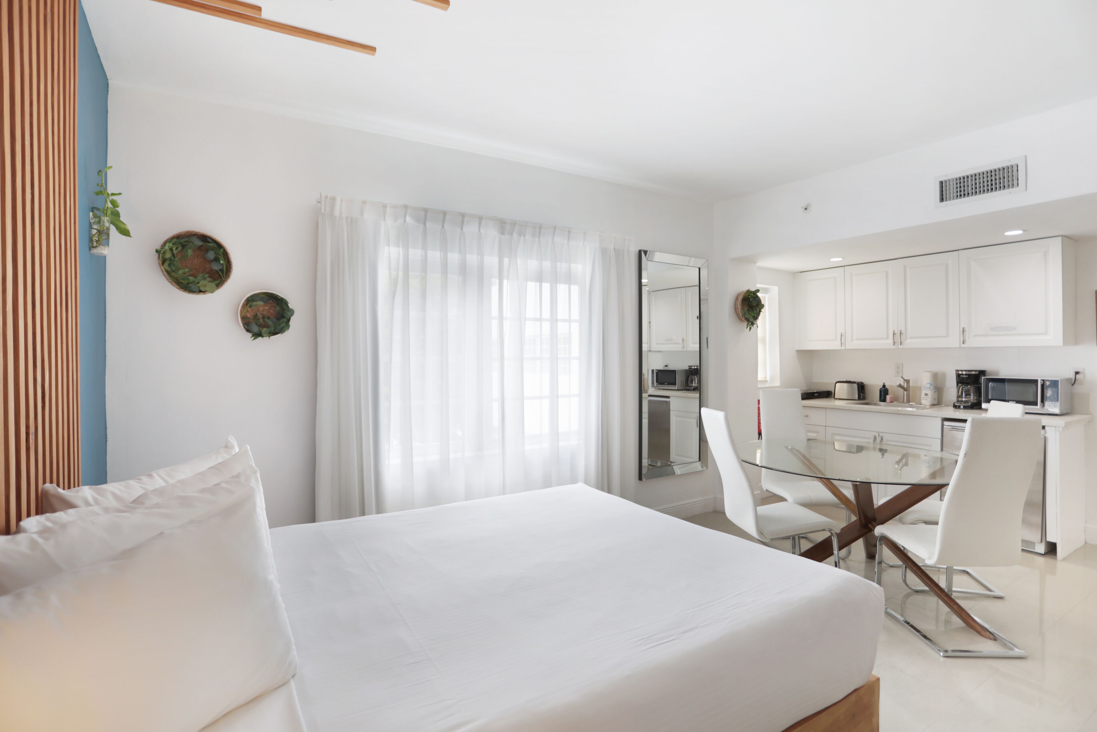 Une chambre d’hôtel moderne avec un grand lit, une table à manger en verre, des murs blancs et un coin cuisine.