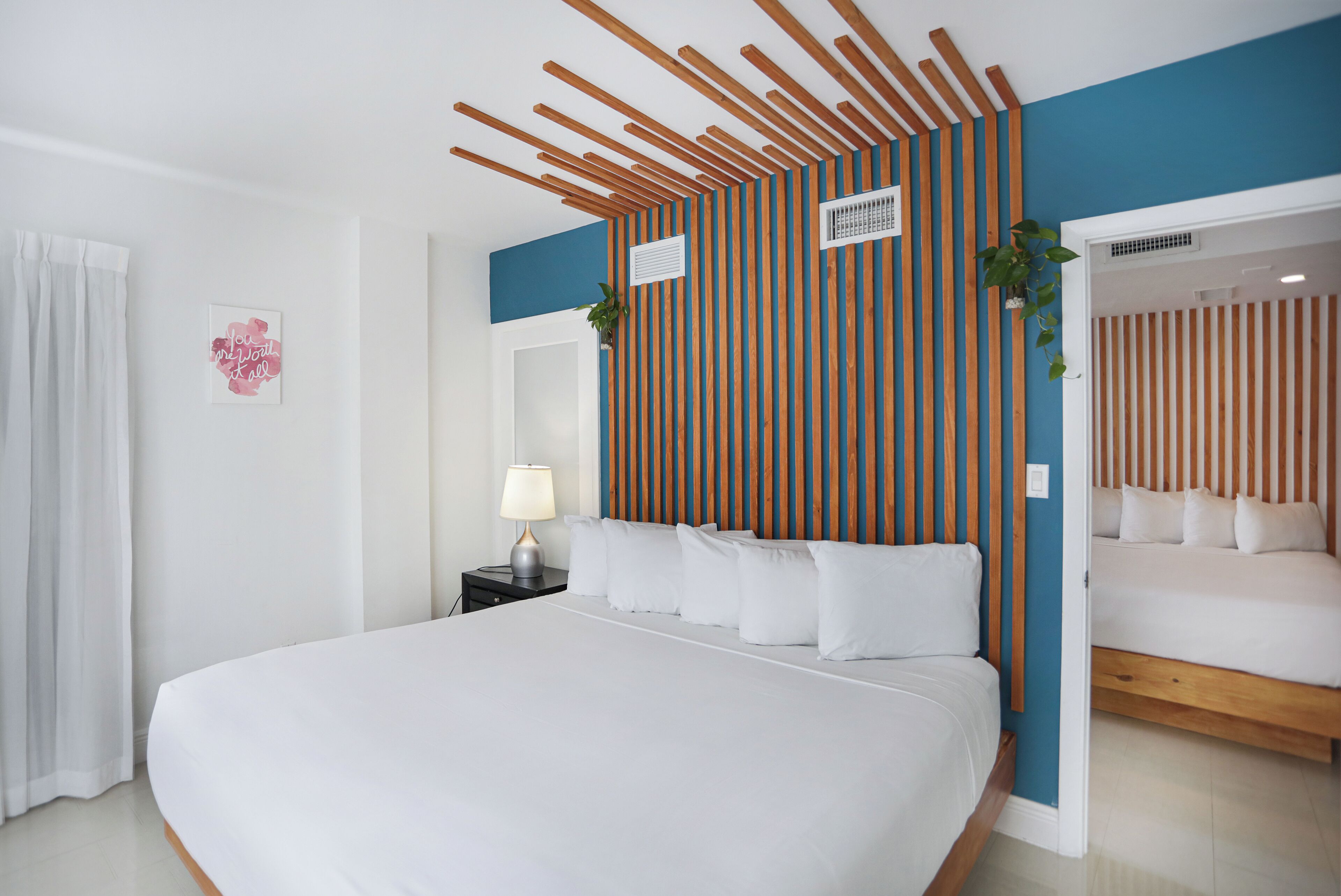 Una habitación de hotel moderna con una cama grande, una mesita de noche con lámpara, un respiradero en la pared y un panel de pared decorativo de listones de madera.